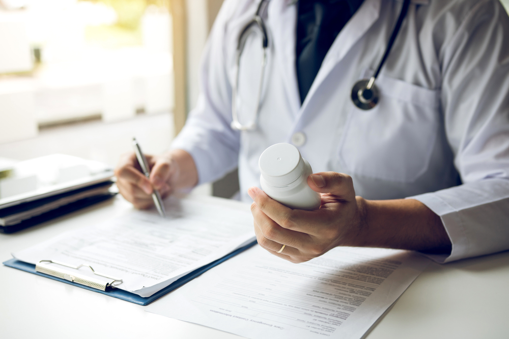 Confident doctor man holding a pill bottle and writing 