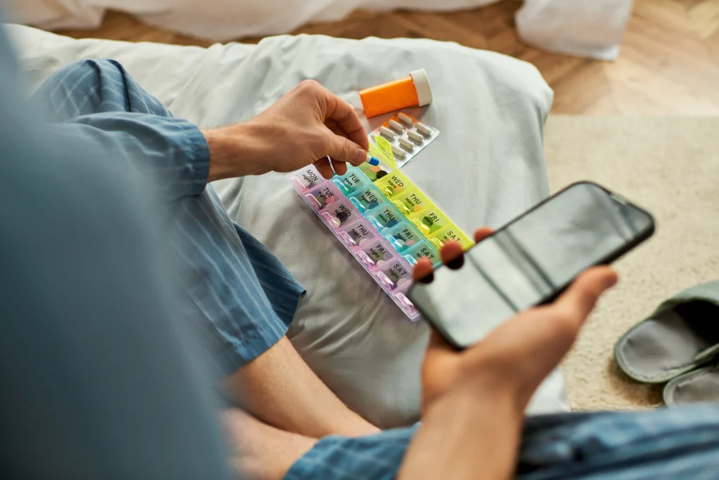 A man organising his pills and setting reminder on his phone to avoid Missing a Dose of Metronidazole.
